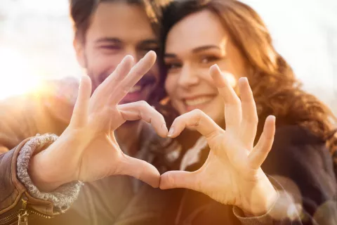 Love coaching, entrenamiento emocional para encontrar pareja Pareja sonríe a la cámara formando con sus manos un corazón