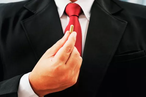 Modafinilo, la pastilla que mejora el rendimiento cognitivo Un hombre con traje sujeta una cápsula con sus dedos