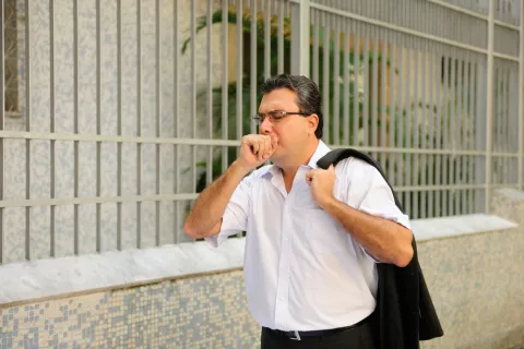 Causas de la tuberculosis Hombre con tuberculosis tose mientras camina por la calle