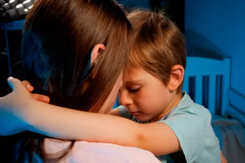 Cómo ayudar a tu hijo a superar el miedo a la oscuridad Madre consolando a su hijo asustado en la cama