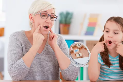 Aconsejan no abandonar las sesiones de logopedia en verano Niña con su logopeda haciendo ejercicios del habla