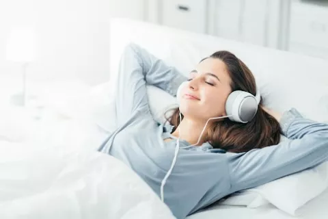 Escuchar palabras relajantes durante el sueño reduce el ritmo cardíaco Chica joven escucha palabras relajantes mientras duerme