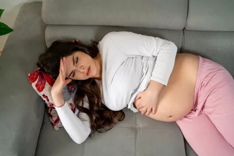 Dormir menos de 7 horas en el embarazo puede retrasar el desarrollo del niño Mujer embarazada tumbada en el sofá porque no puede dormir