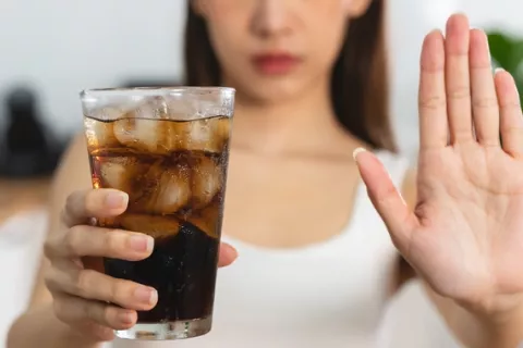 Las bebidas azucaradas aumentan el riesgo cardiovascular y de diabetes Una mujer joven mostrando un vaso con refresco y advirtiendo de sus riesgos